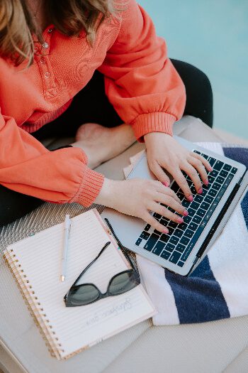 Girl in orange sweatshirt working on computer next to pool
