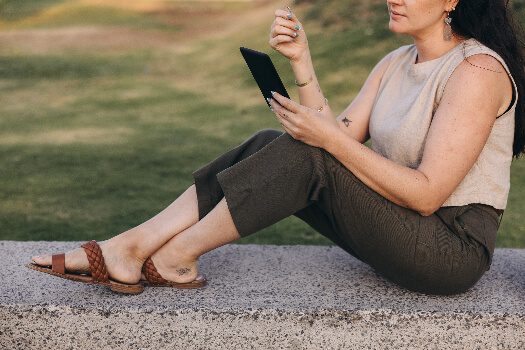 A girl in summer clothes sitting down outdoors and looking at her phone