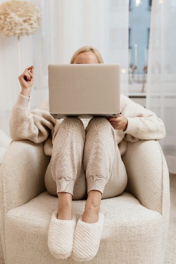 A girl in sweat pants sitting in a chair with her legs up and looking at her computer