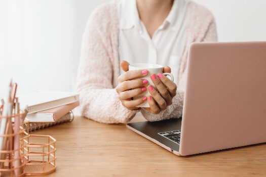 Woman in pink sweater sitting in front of a pink computer and holding a coffee mug