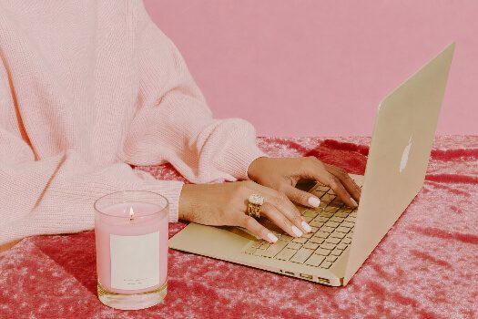 woman typing on computer with a pick background and pink candle