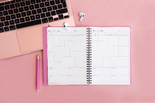 A pink background with a computer and a planning journal on it.