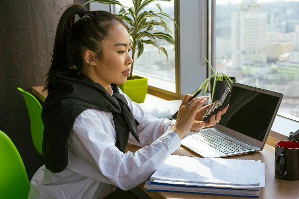 Woman sitting at desk with a large window overlooking the city and she is working on her computer