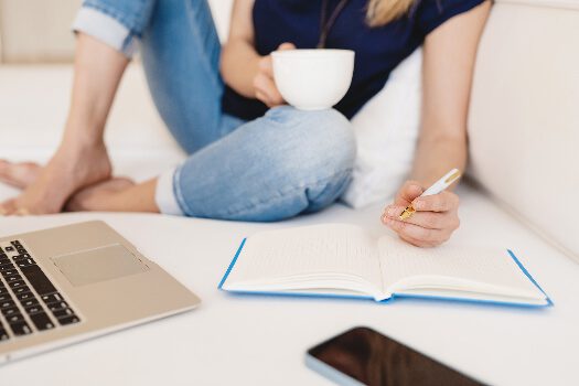 woman sitting on her bed with her computer and writing in a notebook